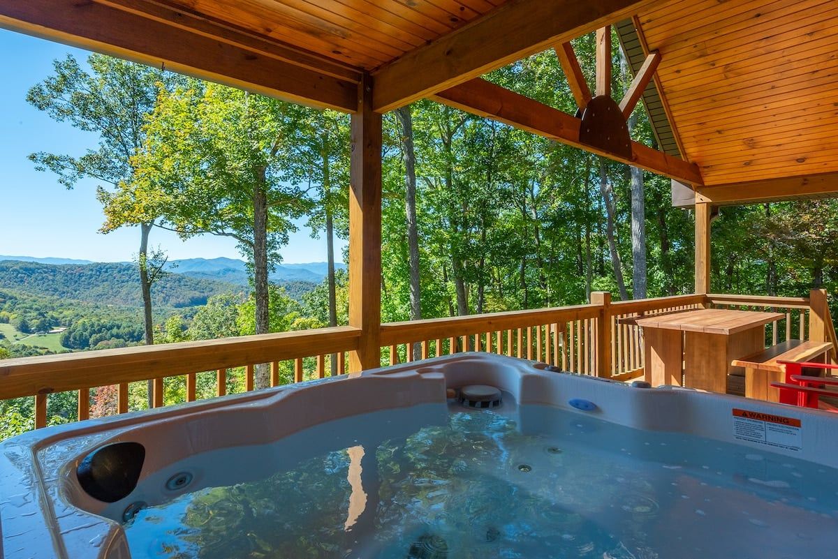 A hot tub on a wooden deck with a view of a forest and mountains.