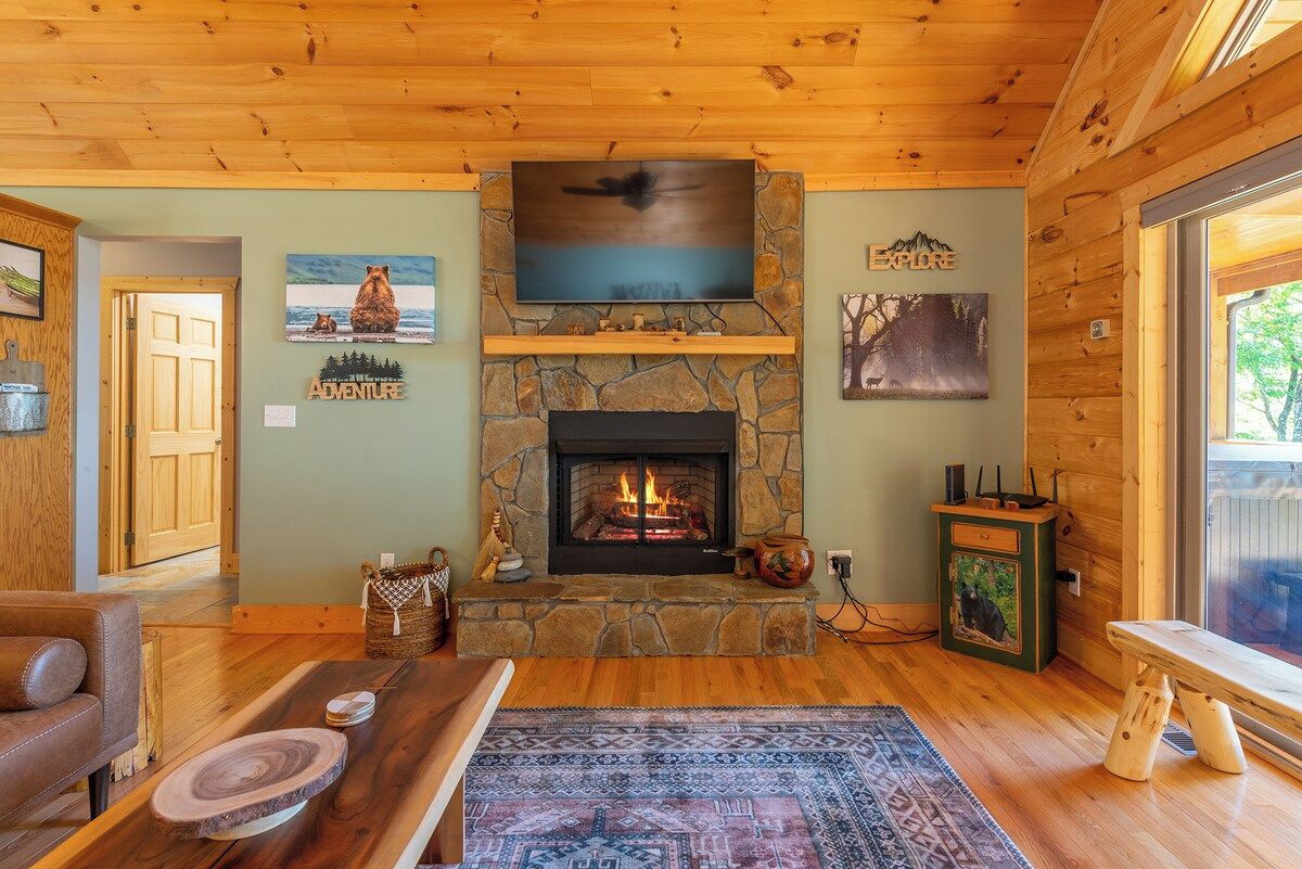 A cozy living room with a stone fireplace, wooden ceiling, and a television mounted above it.