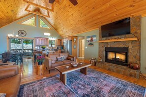 A spacious living room with a fireplace, wooden ceiling, and a dining area visible through an open door. - Stunning Mtn Views, Hot Tub+Fire Pit, WiFi, Grill! (Bakersville)