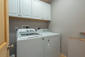 A laundry room with a front-loading washer and dryer, wooden cabinets above, and a tiled backsplash. - Stunning Mtn Views, Hot Tub+Fire Pit, WiFi, Grill! (Bakersville)