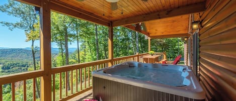 Um deck de madeira com hidromassagem, guarda-corpo de madeira e vista para uma paisagem arborizada.