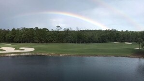 A golf course with sand bunkers, a water body, and a forested area in the background. - Top Floor Condo with Panoramic View of Golf Course & Lake (Naples)