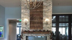 A lobby with a stone fireplace, a chandelier, and a dining area in the background. - Top Floor Condo with Panoramic View of Golf Course & Lake (Naples)