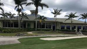 A golf course with a well-maintained lawn, palm trees, and a building with large windows and a dome roof. - Top Floor Condo with Panoramic View of Golf Course & Lake (Naples)
