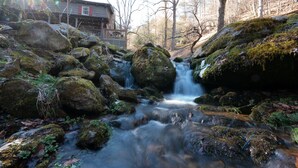 A rustic cabin with a wooden deck and a waterfall in the background. - Blue Ridge Cabin with Modern Farmhouse Decor on Private Stream  (Banner Elk)