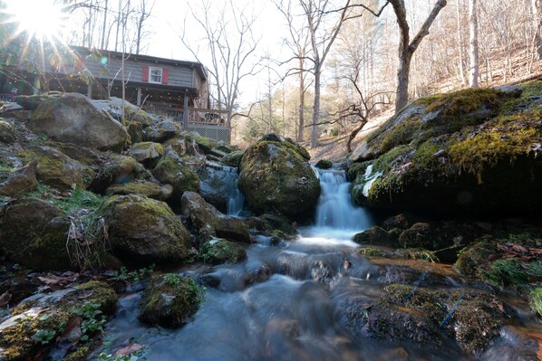 A rustic cabin with a wooden deck and a waterfall in the background.
