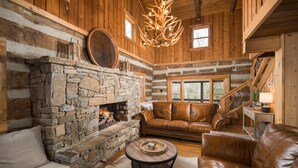 A log cabin interior with a stone fireplace, leather furniture, and a wooden staircase. - Blue Ridge Cabin with Modern Farmhouse Decor on Private Stream  (Banner Elk)