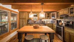 A kitchen with wooden cabinets, a central island with stools, a microwave, stove, and hanging pendant lights. - Blue Ridge Cabin with Modern Farmhouse Decor on Private Stream  (Banner Elk)