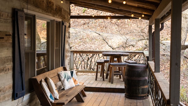 A wooden deck with a bench and table, a barrel, and string lights. - Blue Ridge Cabin with Modern Farmhouse Decor on Private Stream  (Banner Elk)
