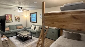 Un lit superposé avec une échelle en bois, un canapé, une table basse, un téléviseur et une horloge au mur.
