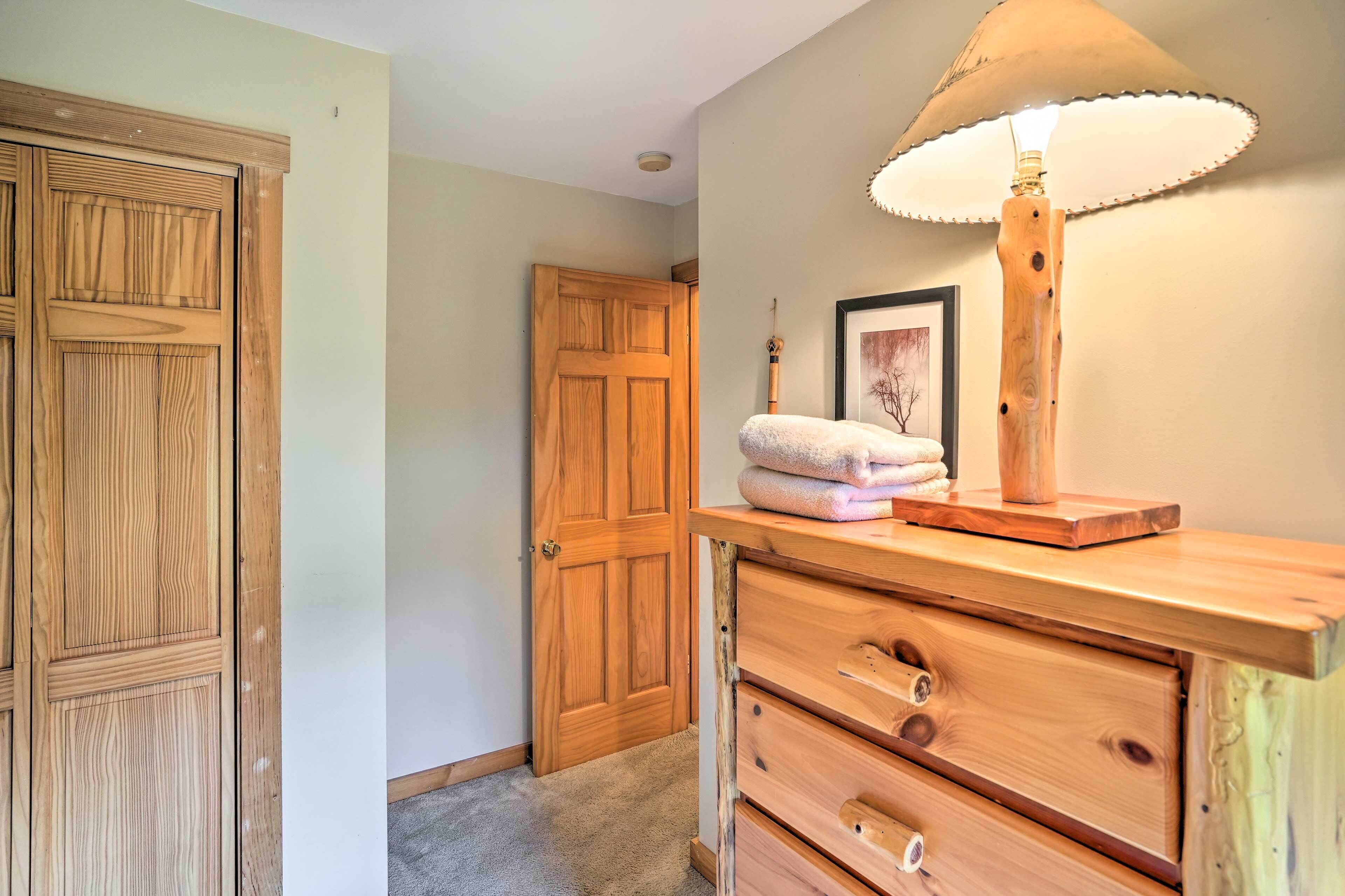 Une commode en bois, avec une lampe, une porte et un tableau encadré accroché au mur.