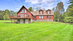 A two-story log cabin with a balcony, surrounded by a well-maintained lawn and trees. - Grand Windham Retreat w/ Fire Pit & Game Room (Windham)