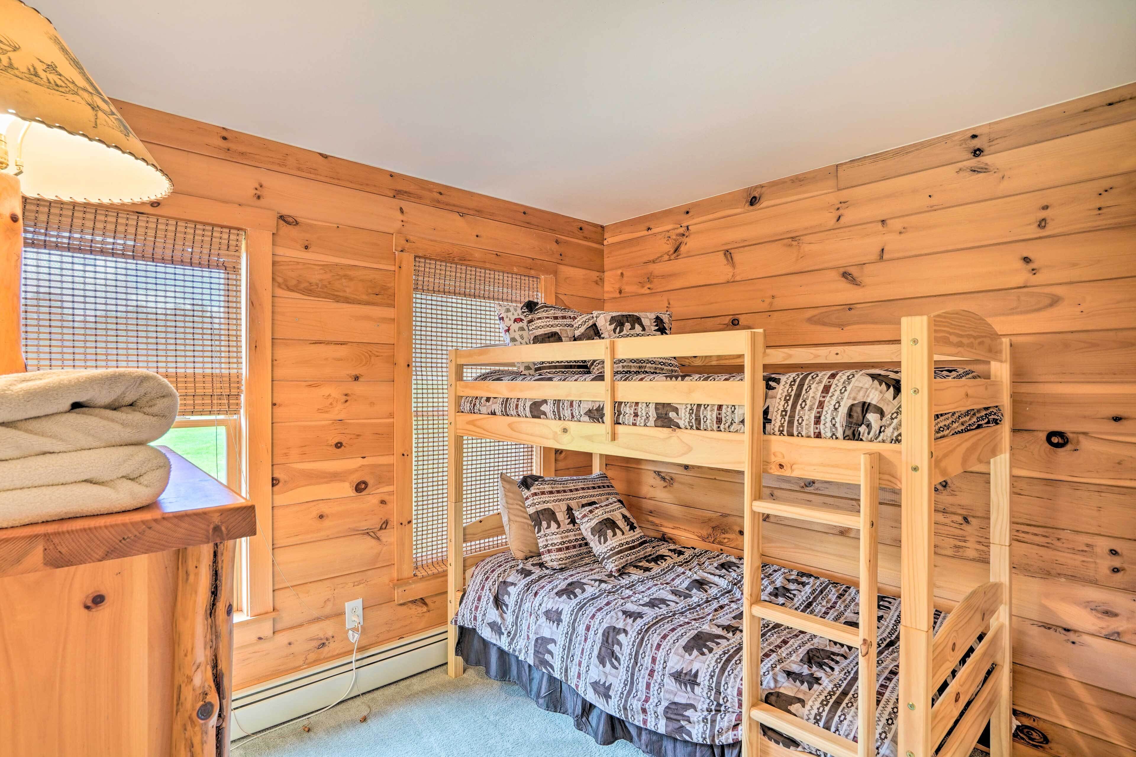 A bunk bed room with wooden walls, a window with blinds, and a lamp on a wooden shelf.