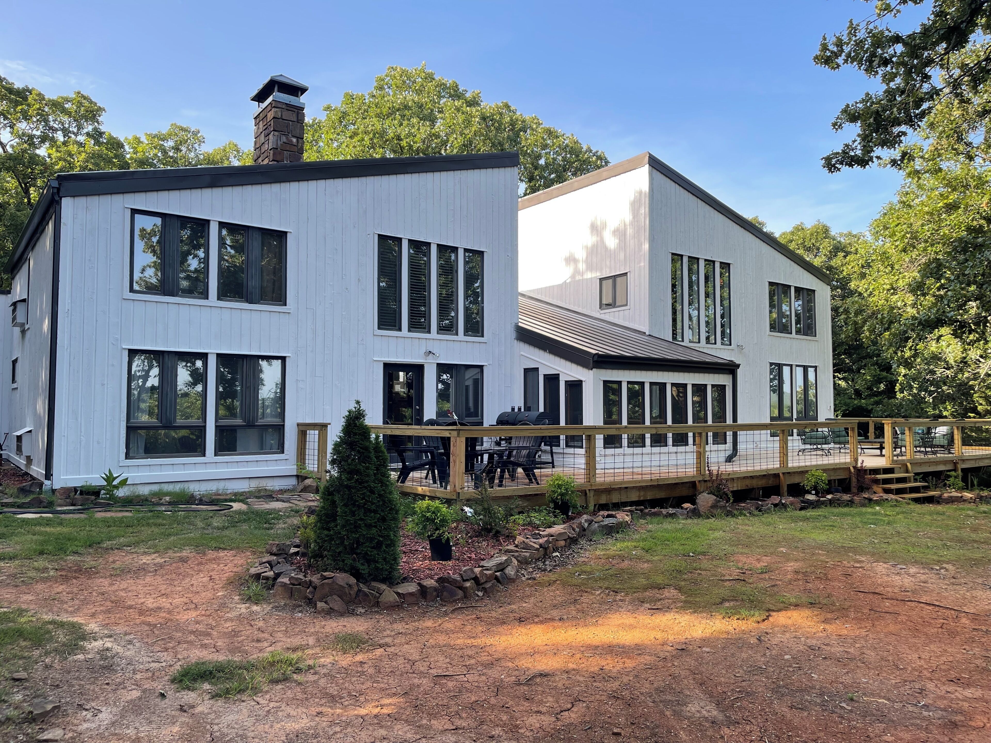 A modern two-story house with large windows, a deck, and a stone chimney.