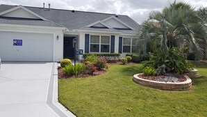 Une maison à deux étages avec un garage, une pelouse bien entretenue et une variété de plantes et d’arbustes.