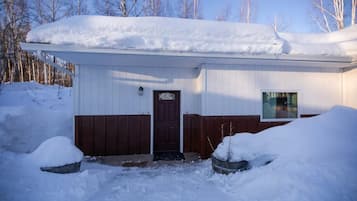 Ein eingeschossiges Gebäude mit brauner Tür und Fenster, umgeben von Schnee.