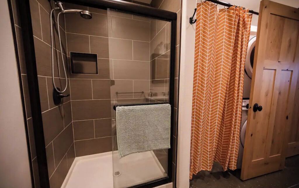 A shower area with a glass door, a towel rack, and a wooden door with a towel hanging on it.