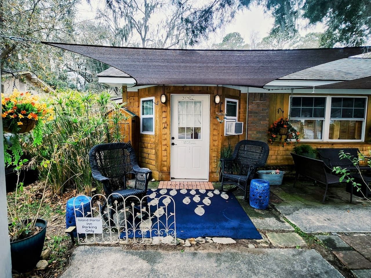A wooden cabin with a porch, two chairs, a blue mat, and a sign indicating parking only.