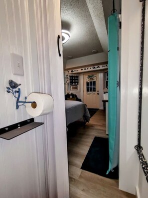 A hallway with a door leading to a bedroom, a toilet paper holder, and a hanging curtain. - Island Parlor Inn Coastal Mid Century Studio (Savannah)