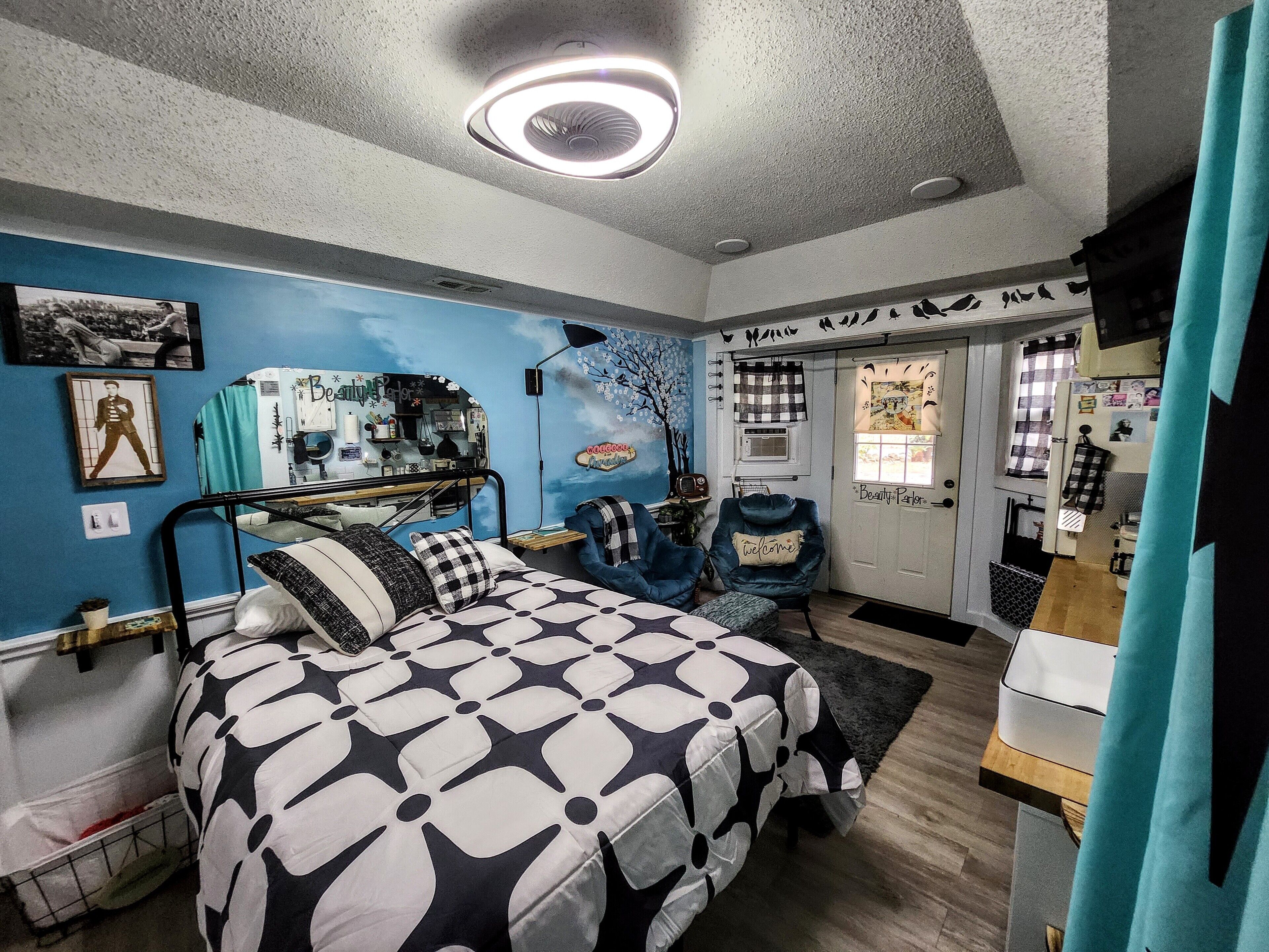 Une chambre avec un lit superposé, un bureau avec une chaise, une coiffeuse avec un miroir et une porte sur laquelle est affiché un panneau « Bienvenue ».