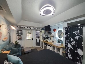 A bedroom with a bed, a desk, a mirror, a TV, and a shower curtain.