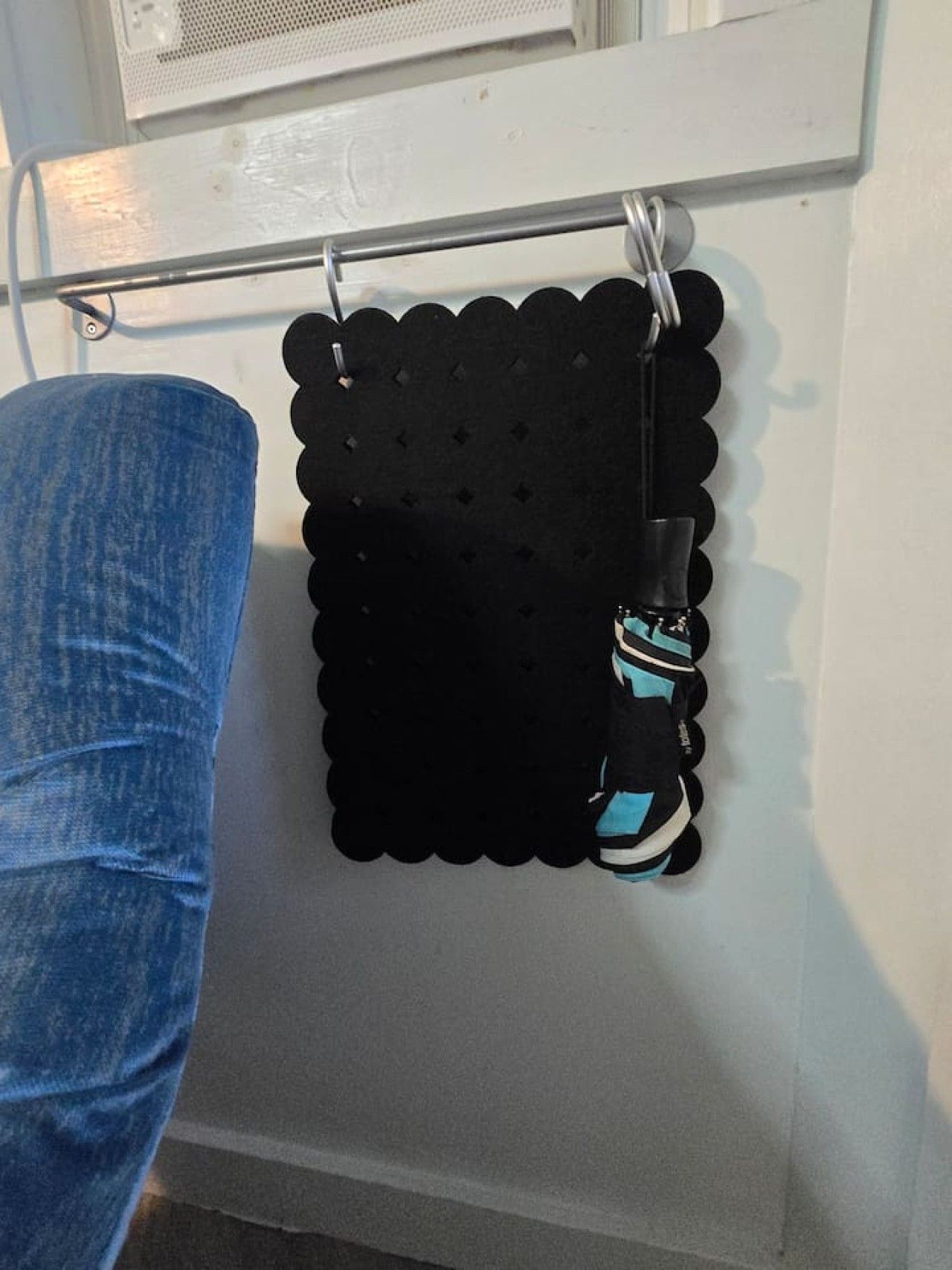 Ein schwarzes, gewelltes Wandbild mit Haken und einem darunter hängenden schwarzen Gegenstand.