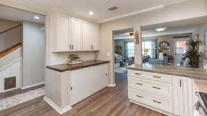 Une cuisine spacieuse avec des meubles blancs, un plan de travail en bois et une vue sur le salon.