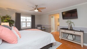 Une chambre avec un lit, un ventilateur de plafond, une télévision, un bureau et une plante.