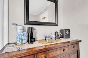 A wooden dresser with a coffee maker, a vintage espresso machine, and a framed mirror above it.