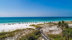 A beach with a wooden walkway leading to the shore, umbrellas, and beachgoers.