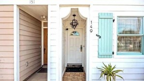 Une maison avec une porte blanche, le numéro « 149 » sur le mur et un pot de fleurs devant.