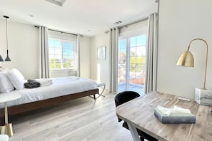 Habitación de hotel moderna con una cama grande, un escritorio de madera y vistas al exterior a través de amplias ventanas.