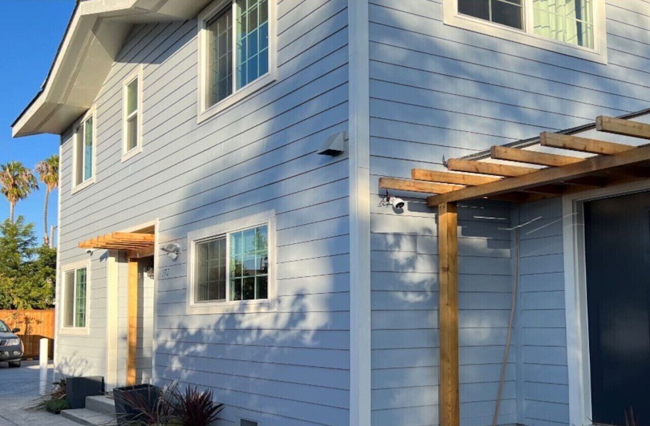 Une maison à deux étages avec un garage, une pergola en bois et un ciel dégagé.