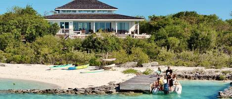 A beachfront property with a large house, a dock, and several boats.