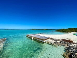A clear blue sea with a wooden pier extending into the water, a sandy beach, and a distant island. - Surf House: 4BR Beachfront w/pool (Hartswell)
