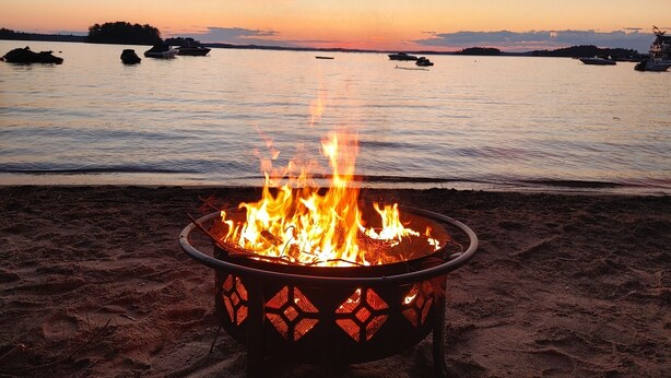 A beach with a fire pit in the foreground and boats on the water in the background. - Sandy Pines Cottage. Lake Muskoka, Gravenhurst (Gravenhurst)