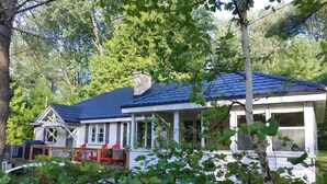 A house with a blue roof, white walls, and a porch with red chairs. - Sandy Pines Cottage. Lake Muskoka, Gravenhurst (Gravenhurst)