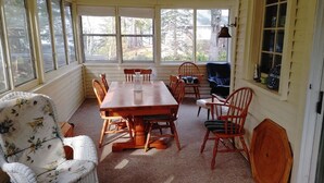 A sunroom with a wooden table and chairs, large windows, and a view of the outdoors. - Sandy Pines Cottage. Lake Muskoka, Gravenhurst (Gravenhurst)