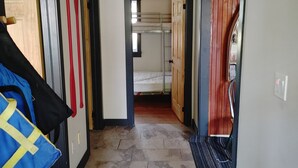 A hallway with a bunk bed in the background, a blue bag on the floor, and a wooden ceiling. - Sandy Pines Cottage. Lake Muskoka, Gravenhurst (Gravenhurst)