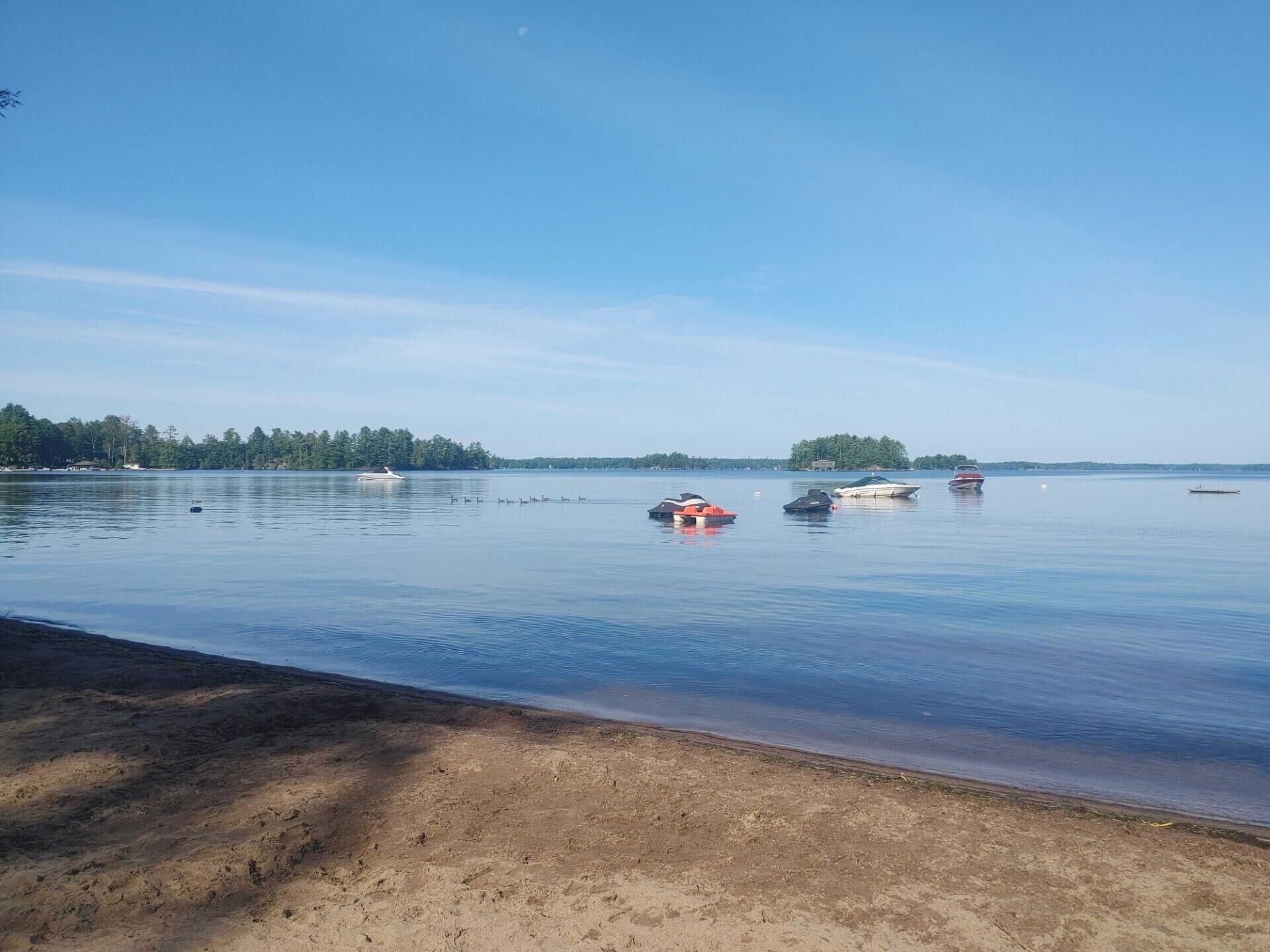 A calm lake with several boats and a sandy beach.