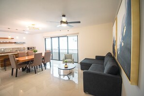 A modern living room with a dining area, a ceiling fan, and a large window with a view.