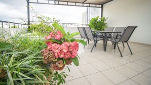 Un espace extérieur abrité, doté d’une table et de chaises, et entouré de plantes et de fleurs.