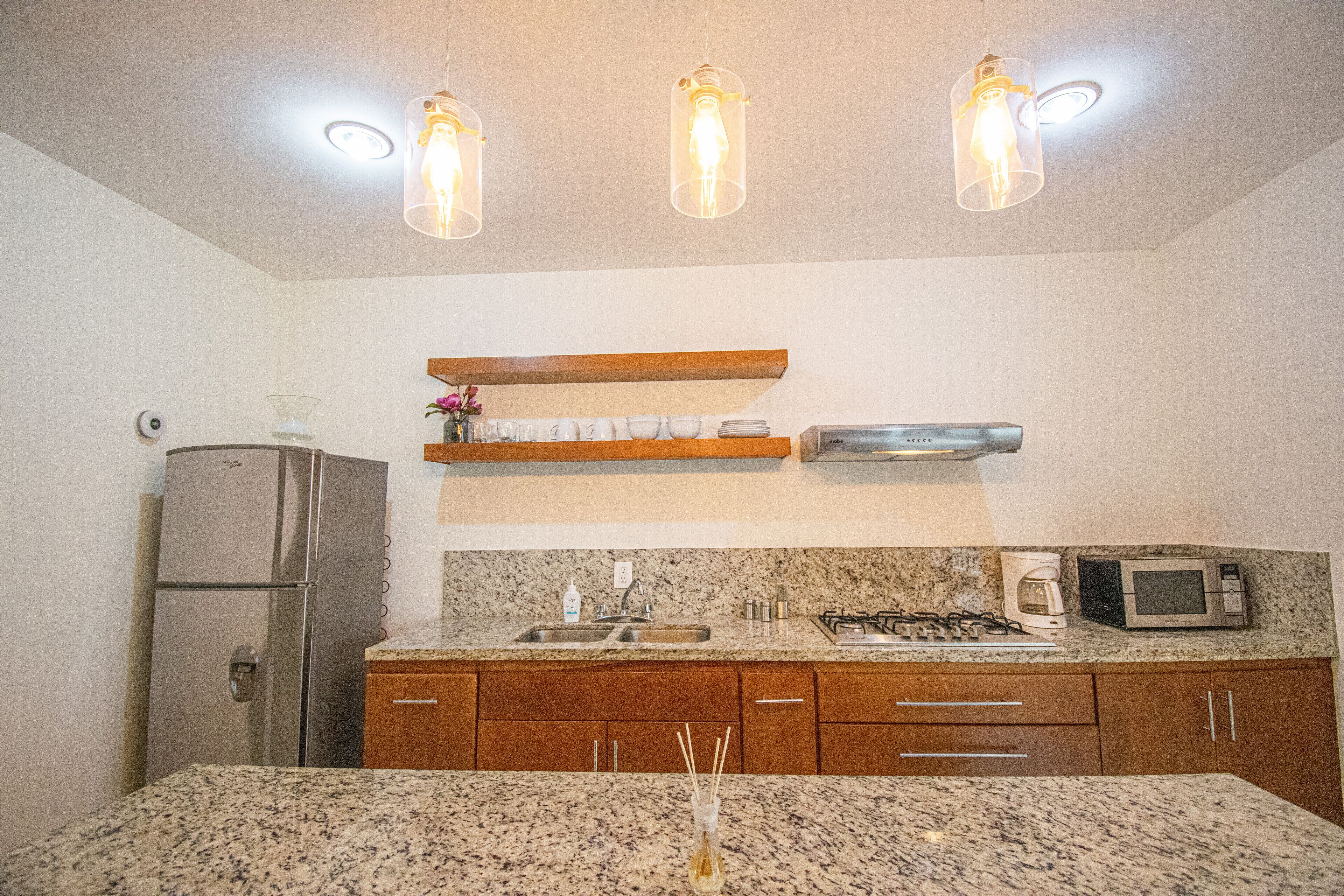 A kitchen with granite countertops, stainless steel appliances, wooden cabinets, and pendant lighting.