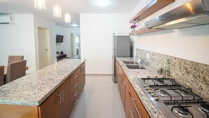 Une cuisine moderne dotée de plans de travail en granit, d’appareils électroménagers en acier inoxydable et de luminaires suspendus.