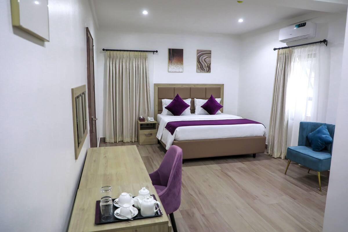 Habitación de hotel con cama, escritorio con juego de té, una silla y un sillón azul.