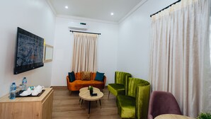 Una sala moderna con un sofá, sillones verde y morado, una mesa de centro de madera y un escritorio pequeño con una bandeja de objetos.
