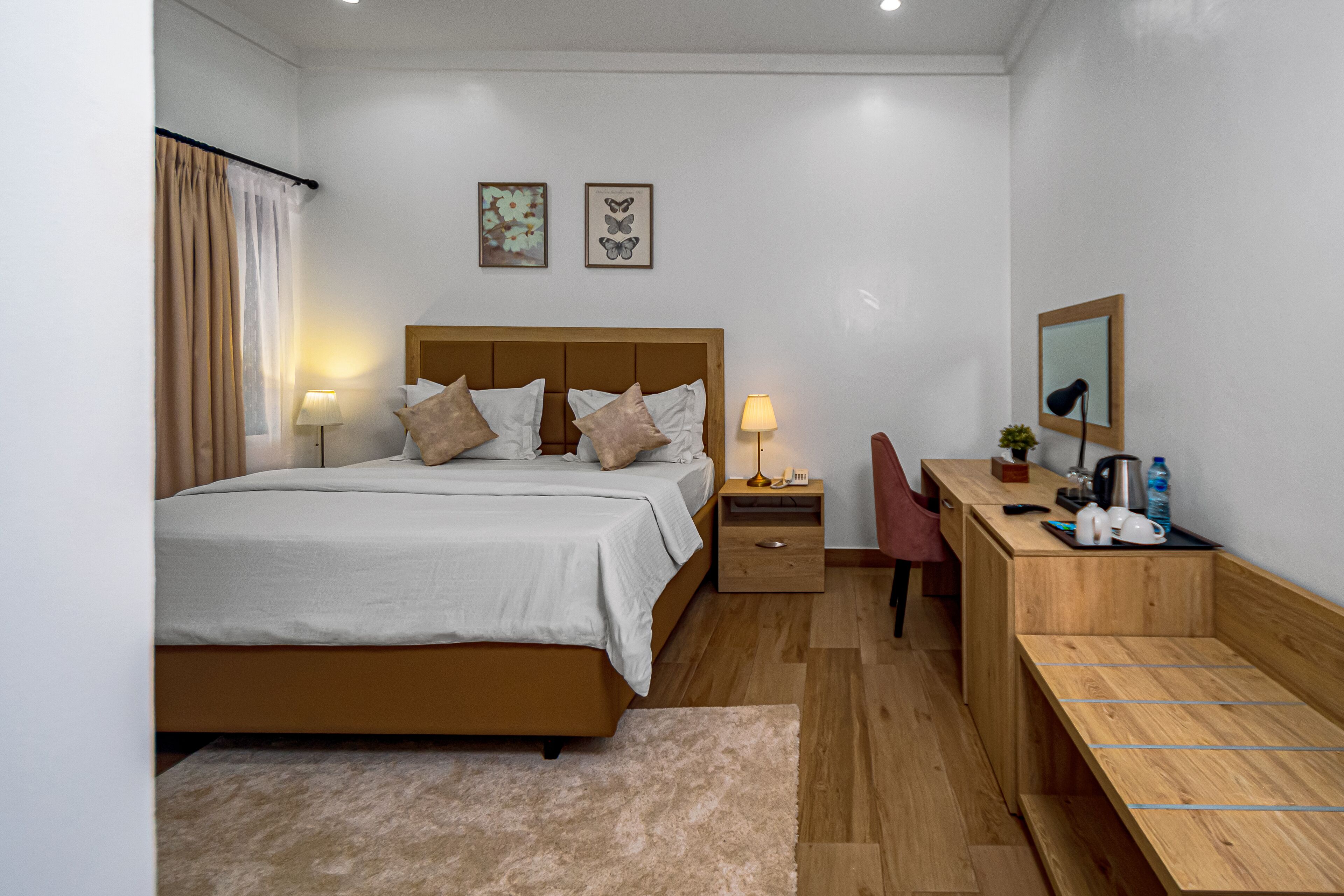 A modern hotel room with a large bed, bedside tables, a desk with a chair, a mirror, and artwork on the wall.