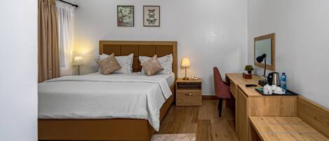 A modern hotel room with a large bed, bedside tables, a desk with a chair, a mirror, and artwork on the wall.