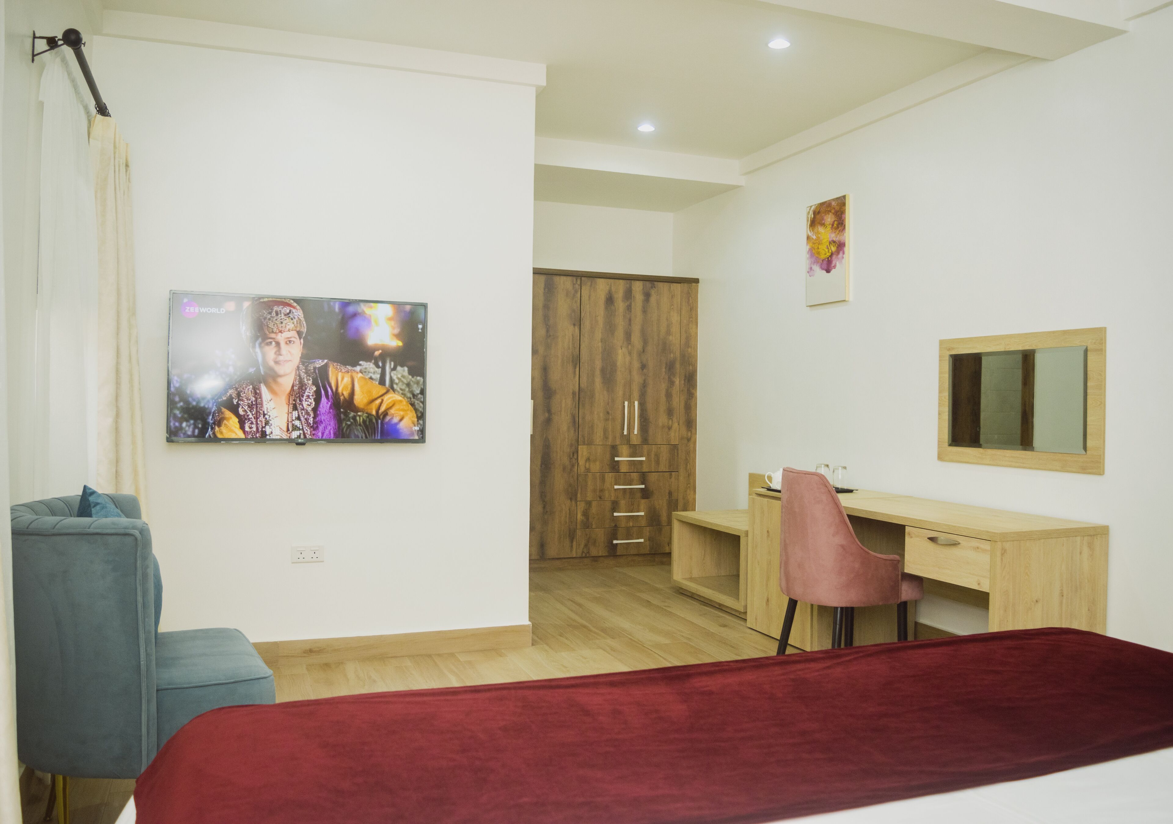 A bedroom with a bed, a desk, a chair, a wardrobe, a television, and a painting on the wall.