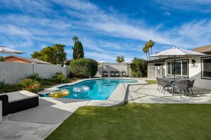 A backyard with a swimming pool, lounge chairs, and a patio table.